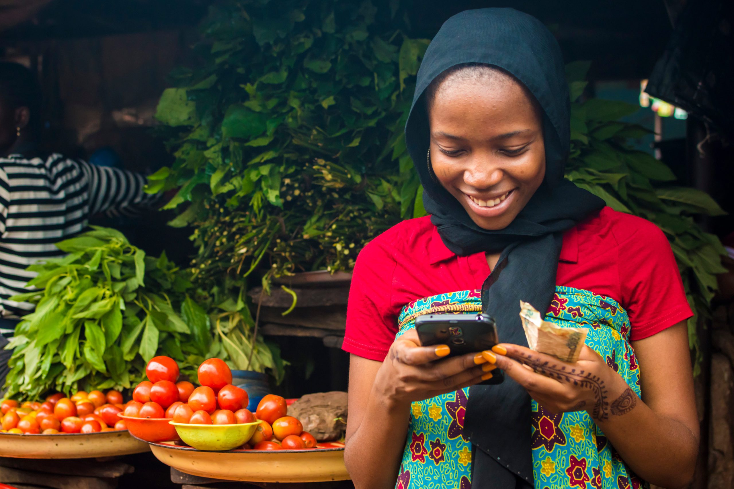 young african woman selling in a local market smiling while using her mobile phone